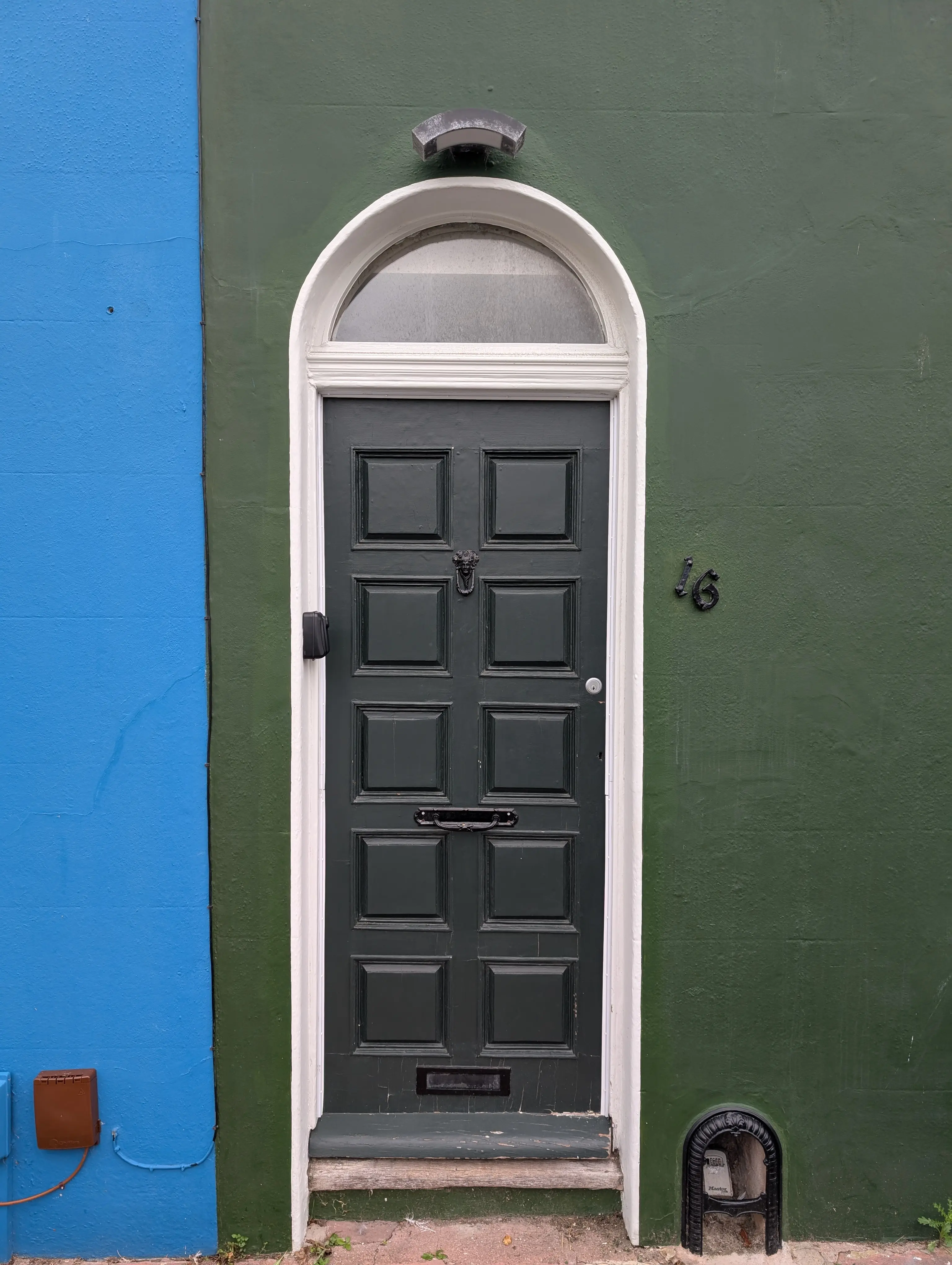 black door with square panelling on dark green wall